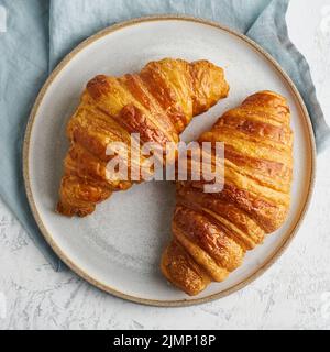 Due deliziosi croissant su piatto e bevanda calda in tazza. Colazione francese al mattino Foto Stock