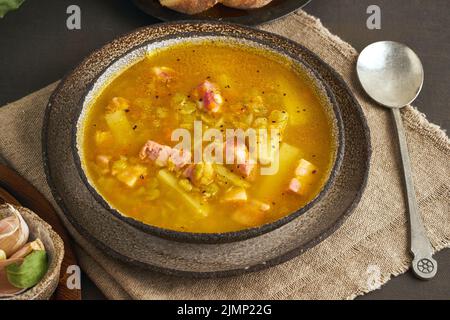 Zuppa calda invernale con piselli verdi tritati, maiale, pancetta, affumicata su tavolo di legno marrone scuro. Deliziosa zuppa ricca di grassi. Foto Stock