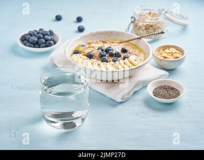 Bicchiere di acqua pulita e una sana colazione con farinata d'avena, mirtilli, banana Foto Stock