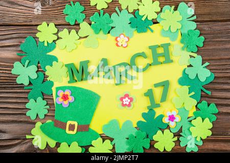 Happy Saint Patrick's greeting card mockup del feltro a mano hat e shamrock clover le foglie e i fiori sul tavolo in legno Foto Stock