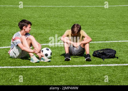 I bambini parlano allo stadio della scuola all'aperto. Ragazzo adolescente confortante consolante sconvolto triste amico. Educazione, intimidazione, conflitto, relazioni sociali Foto Stock