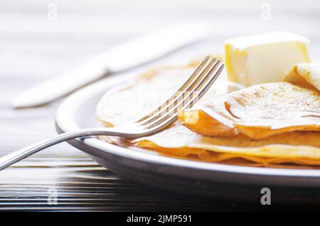 Pila di crepes francese con il burro nel piatto di ceramica su legno tavolo da cucina Foto Stock