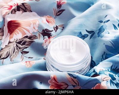 Cosmetici per la cura della pelle, crema viso vaso idratante su sfondo floreale blu, prodotto di bellezza flatlay primo piano Foto Stock