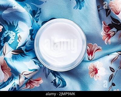 Cosmetici per la cura della pelle, crema viso crema idratante vaso su sfondo floreale blu, prodotti di bellezza flatlay Foto Stock