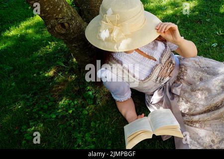 Una donna in un bel vestito tradizionale bavarese dirndl (o Tracht) leggendo un libro sul prato verde in una giornata estiva soleggiata (Monaco, Baviera, tedesco Foto Stock