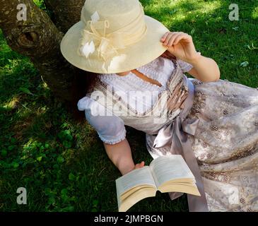 Una donna in un bel vestito tradizionale bavarese dirndl (o Tracht) leggendo un libro sul prato verde in una giornata estiva soleggiata (Monaco, Baviera, tedesco Foto Stock