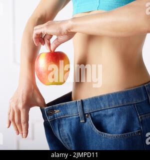 Caucasian modello femminile in jeans blu con mela rossa mostra la sua pancia piatta. Uno stile di vita sano e Weightloss concetto. Foto Stock