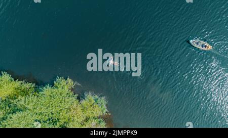 Vista aerea di un uomo che nuota in un fiume seguita da un paio di kayak in un kayak su acque turchesi. Drone shot uccelli vista occhio. Fiume Wharfe Foto Stock