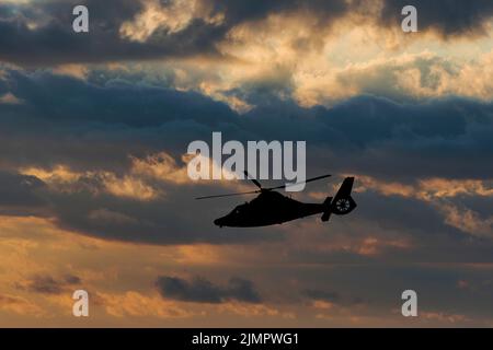 Un elicottero della Guardia Costiera degli Stati Uniti in silhouette contro un cielo nuvoloso in un'immagine composita. Foto Stock