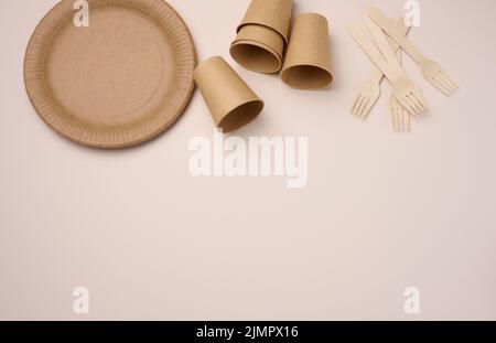 Tazze e piatti di carta marroni su sfondo beige. Rifiuti riciclabili, rifiuto di plastica, vista dall'alto Foto Stock