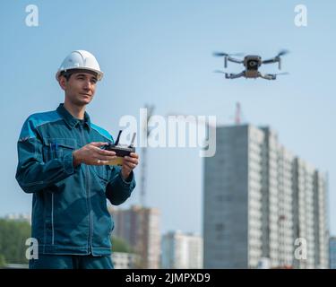 Un uomo in un casco e tute controlla un drone in un cantiere. Il costruttore esegue la supervisione tecnica. Foto Stock