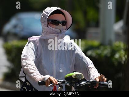 Fuyang, Cina. 07th ago 2022. Una donna va in bicicletta indossando un cappello, una maschera e occhiali da sole durante il tempo caldo. Secondo le previsioni dell'Osservatorio Meteorologico Centrale della Cina, nei prossimi 10 giorni, le alte temperature continueranno in alcune parti della Cina, con la temperatura massima che raggiunge i 37-39 ° C e la temperatura locale di 40 ° C o superiore. Credit: SOPA Images Limited/Alamy Live News Foto Stock