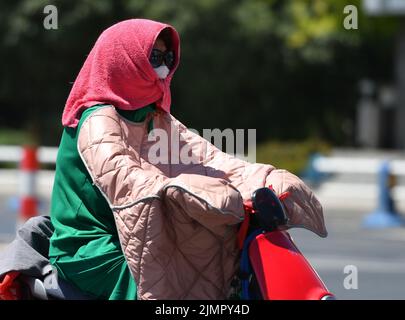 Fuyang, Cina. 07th ago 2022. Una donna guida una moto scooter mentre copre la testa con un asciugamano durante il tempo caldo. Secondo le previsioni dell'Osservatorio Meteorologico Centrale della Cina, nei prossimi 10 giorni, le alte temperature continueranno in alcune parti della Cina, con la temperatura massima che raggiunge i 37-39 ° C e la temperatura locale di 40 ° C o superiore. Credit: SOPA Images Limited/Alamy Live News Foto Stock