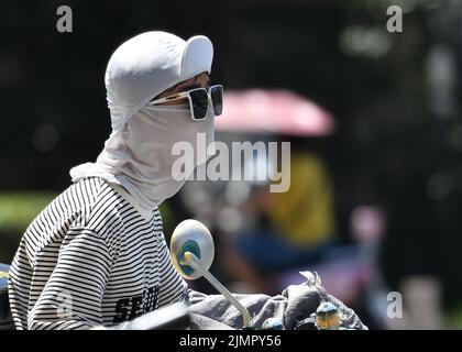 Fuyang, Cina. 07th ago 2022. Una donna che guida una bicicletta indossa una maschera bianca e occhiali da sole durante il tempo caldo. Secondo le previsioni dell'Osservatorio Meteorologico Centrale della Cina, nei prossimi 10 giorni, le alte temperature continueranno in alcune parti della Cina, con la temperatura massima che raggiunge i 37-39 ° C e la temperatura locale di 40 ° C o superiore. Credit: SOPA Images Limited/Alamy Live News Foto Stock