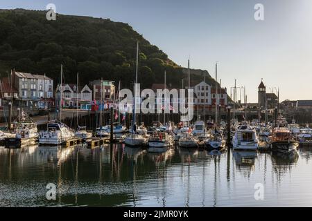 Sole di prima mattina che illumina le barche e gli yacht ormeggiati nel porto di Scarborough, con il Castello di Scarborough sullo sfondo. Foto Stock