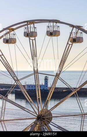 Una vista del faro del porto e del molo attraverso la Big Wheel sulla South Bay di Scarborough, sulla costa settentrionale dello Yorkshire. Foto Stock