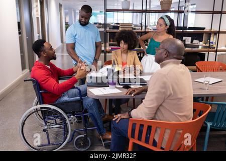 Disabili giovane uomo d'affari afroamericano che discute con i colleghi biraciali in riunione Foto Stock