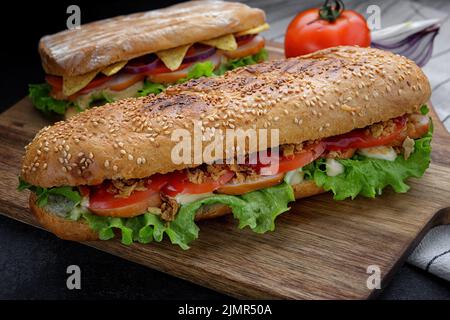 Sandwich con carne affumicata, formaggio e pomodori su un pannello di legno sullo sfondo di un altro sandwich Foto Stock