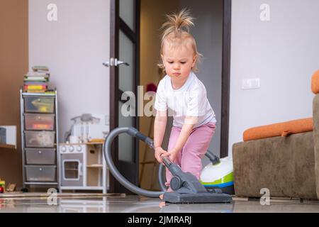 Piccola figlia pulizia in casa, bambino spolverare, carino piccola helper ragazza lavaggio pavimento con mop, la famiglia felice pulisce la camera, Foto Stock