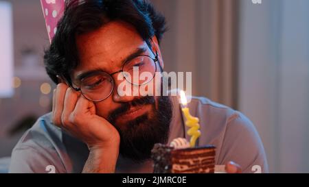 Headshot arabian da solo singolo triste sconvolto solitario indiano ported uomo in festive compleanno rosa cappello e bicchieri seduti a casa di notte sentirsi frustrato Foto Stock