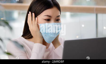 Confuso donna asiatica in maschera medica lettura cattive notizie su covid19 pandemic ricevere e-mail di rifiuto su laptop depresso stress spiacevole errore online Foto Stock