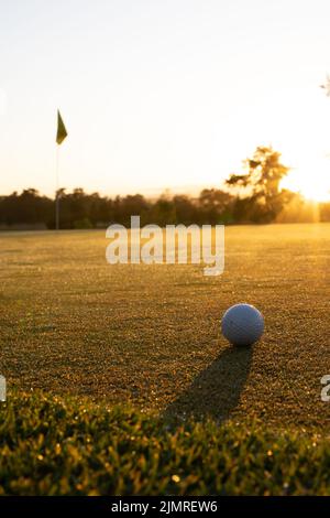 Palla da golf su paesaggio erboso contro alberi e cielo limpido durante il tramonto, spazio copia Foto Stock