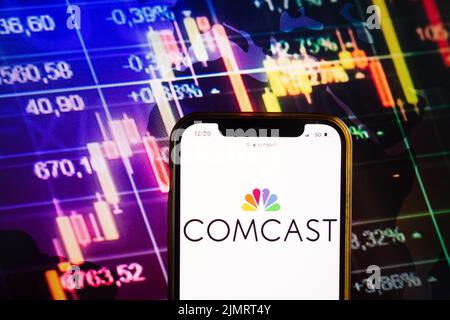 KONSKIE, POLONIA - 07 agosto 2022: Smartphone con logo Comcast Corporation sullo sfondo del diagramma di borsa Foto Stock