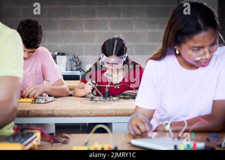 Un gruppo di studenti del college tecnico sono in classe a studiare, esercitando a saldare pezzi di hardware su una scheda a circuito stampato. Concetto di superiore Foto Stock