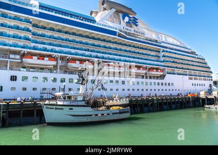 Una barca da pesca legata accanto alla gigantesca nave da crociera Coral Princess ai moli delle navi da crociera nel centro di Ketchikan, Alaska. Foto Stock