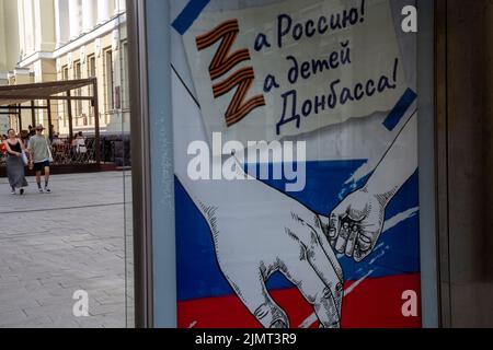 Mosca, Russia. 7th agosto 2022. La gente cammina da un cartellone pubblicitario sociale che mostra le lettere Z - un'insegna tattica delle truppe russe in Ucraina e la lettura 'per la Russia! Per i bambini di Donbass!' Nel centro di Mosca, Russia Foto Stock