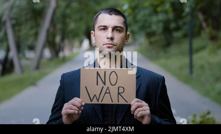 Grave forte attivista caucasico uomo adulto in piedi all'aperto dimostrando cartoncino con parole nessuna guerra che protestano contro l'invasione russa Foto Stock