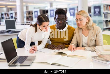 Tutor femminile che aiuta gli studenti a prepararsi per l'esame in biblioteca Foto Stock