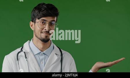 Arabo indiano ragazzo giovane maschio medico professionista uomo tenere spazio copia sulla palma puntando a spazio di lavoro mockup promo luogo per l'offerta di immagine della pubblicità Foto Stock