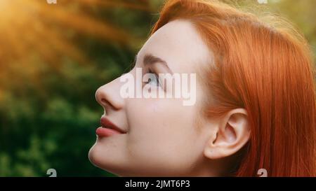 Primo piano femmina ispirato grazioso profilo faccia attraente modello adolescente bella redhead ragazza si alza fuori raggi di sole tramonto sfondo giovane sognante Foto Stock