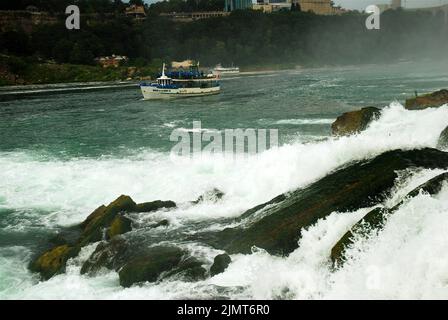 I passeggeri del tour in barca Maid of the Mist indossano impermeabili a poncho blu mentre navigano davanti alle American Falls nelle Cascate del Niagara Foto Stock