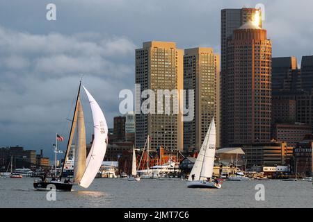 Una regata di barche a vela scivola oltre il Boston Skyline e attraverso il porto di Boston in una calda giornata estiva soleggiata Foto Stock