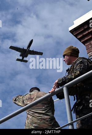 Un aereo A-10C Thunderbolt II assegnato al 104th Fighter Squadron, Maryland Air National Guard, vola oltre due membri del servizio degli Stati Uniti presso la gamma Kazlų Rūda in Lituania durante IL DEFENDER-Europe 22, 19 maggio 2022. L'annuale esercizio congiunto su larga scala e multinazionale guidato dall'esercito statunitense mira a costruire la disponibilità e l'interoperabilità tra gli Stati Uniti, la NATO e i militari partner. (STATI UNITI Foto della Guardia Nazionale aerea di Capt. Benjamin Hughes) Foto Stock