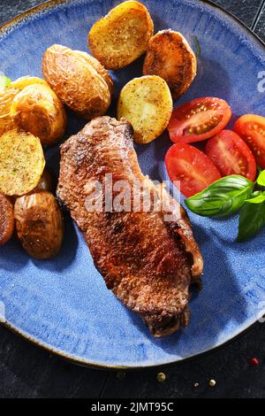 Bistecca di manzo fritta in padella con patate fritte e pomodori ciliegini. Foto Stock