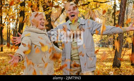 Felice sposato anziano coppie caucasiche partner nel parco civile donna matura uomo anziano spargimento fogliame all'aperto gettare in autunno caduto foglie bella pe Foto Stock