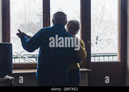 Dolce anziano europeo sposato coppia abbracciando e ballando nel buio soggiorno, tenendo le mani, godendo di riposo insieme durante le fredde giornate invernali. Foto di alta qualità Foto Stock