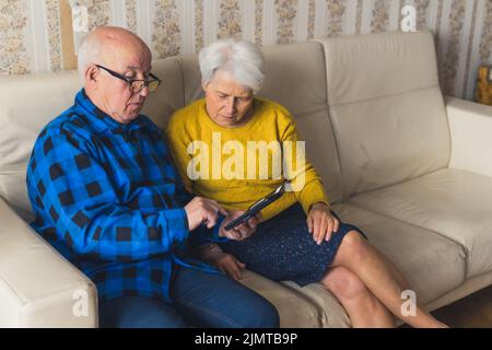 Caucasica senior confuso coppia cercando di imparare a utilizzare uno smartphone mentre si siede su un divano in salotto. Foto di alta qualità Foto Stock