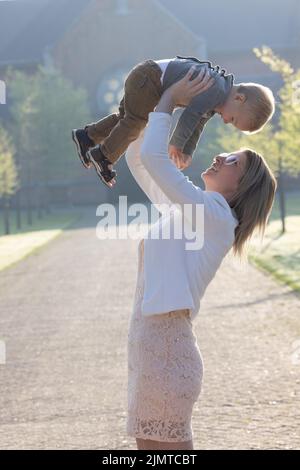 Una giovane e felice madre e un bambino, giocando, si trovano al centro di un parco ai raggi del sole del mattino Foto Stock