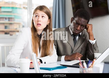 Manager insoddisfatti che lavorano con notebook e documenti al tavolo in ufficio Foto Stock