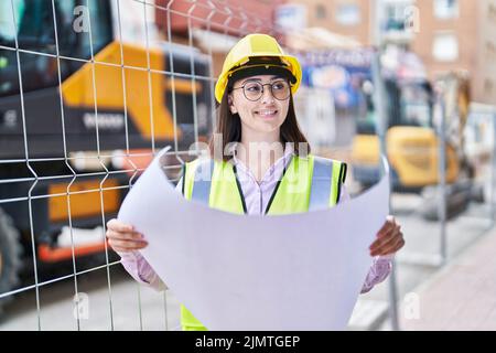 Giovane donna ispanica architetto lettura piani in strada Foto Stock