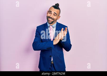 Giovane uomo ispanico che indossa abito da lavoro e cravatta applaudendo felice e gioioso, sorridendo mani fiere insieme Foto Stock