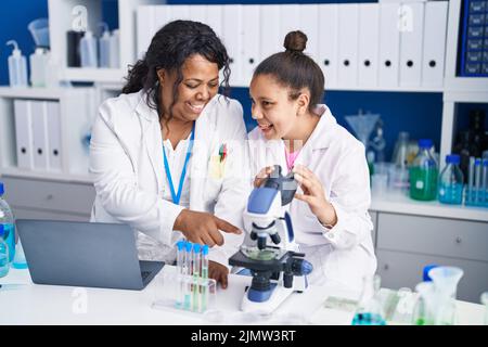 Madre e figlia scienziati che utilizzano microscopio e laptop che lavorano in laboratorio Foto Stock