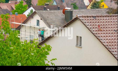 Costruzione di case. Riparazione del tetto e sostituzione delle piastrelle. Costruttori su impalcature su background.The città costo di costruzione in Europa. Foto Stock