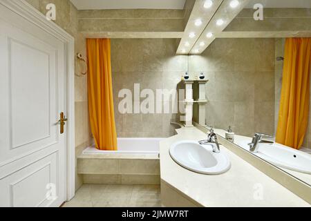 Bagno con ripiani in marmo color crema, grande specchio senza cornice su una parete e lavandino in porcellana bianca Foto Stock