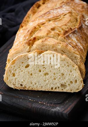 Pane ovale intero cotto a base di farina di grano bianco su un tavolo nero, dolci freschi Foto Stock