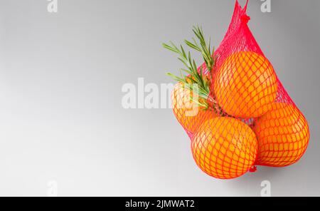 Fondo grigio con arance e rametto di rosmarino in un sacchetto a rete, formato orizzontale Foto Stock